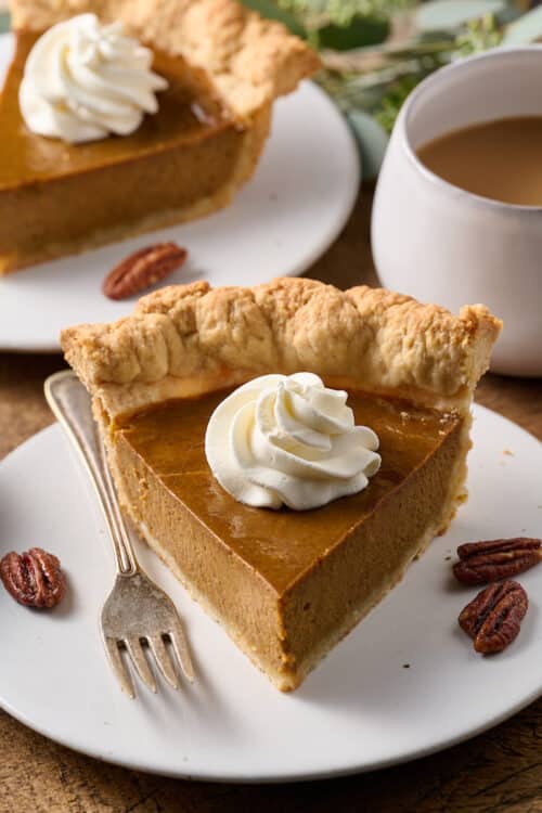 Slice of pumpkin pie on a plate with whipped cream on top.