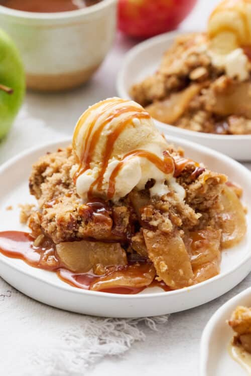 Apple crisp topped with a drizzle of caramel sauce and vanilla ice cream. on a plate.