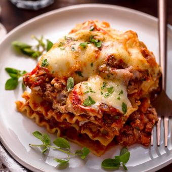 A slice of lasagna on a plate with a glass of wine.